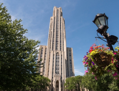 the Cathedral of Learning in front of a blue sky, surrounded by greenery